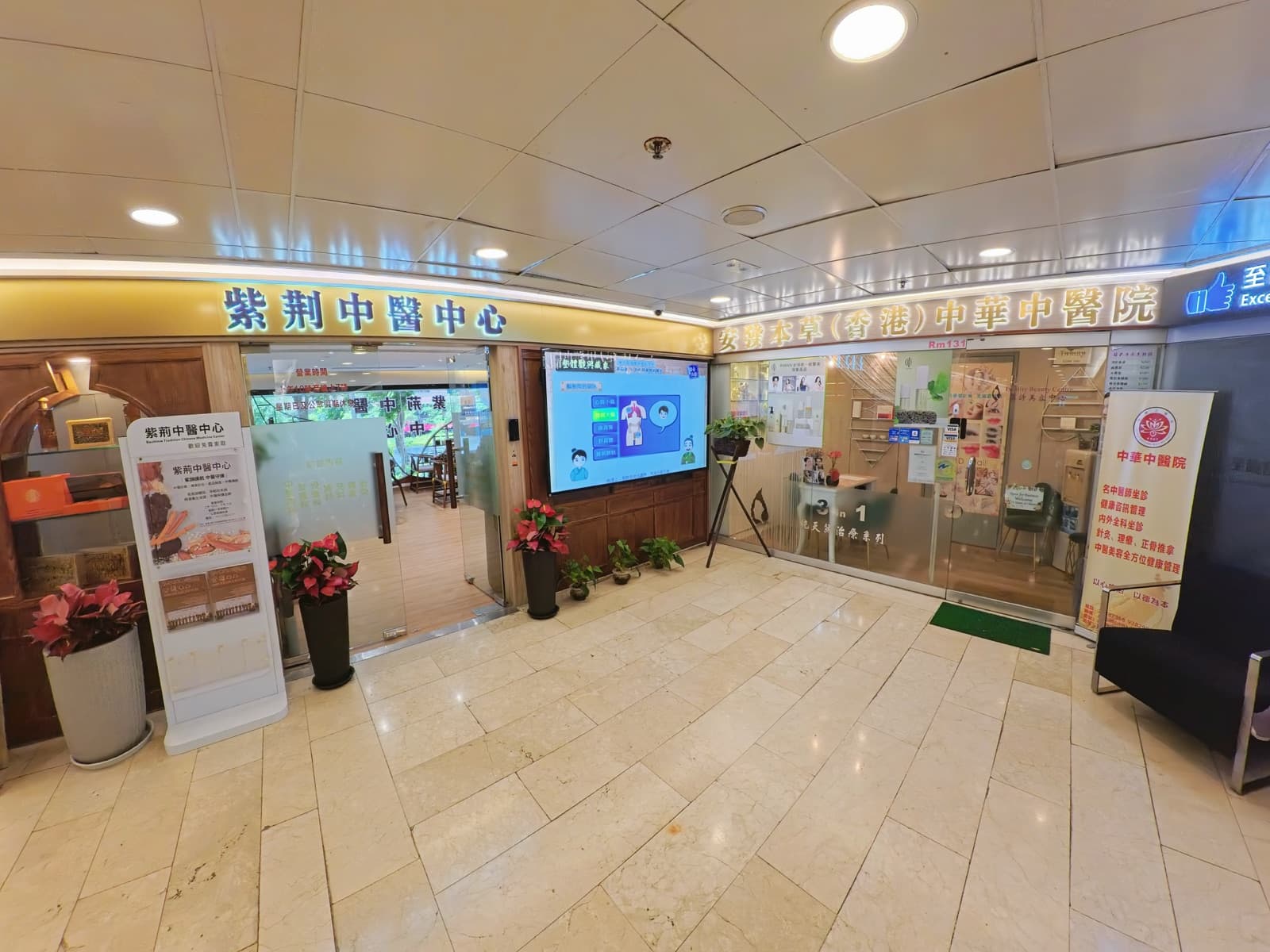 本院於半島中心商場內的店面,左方招牌為紫荊中醫中心,右方招牌為安發本草(香港)中華中醫院,門外設有花卉及資訊屏幕。